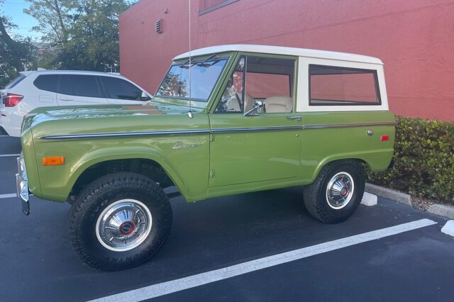 A green and white bronco parked in a parking lot.
