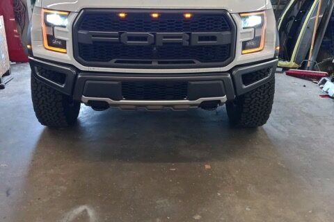 A white truck parked in a garage with its lights on.